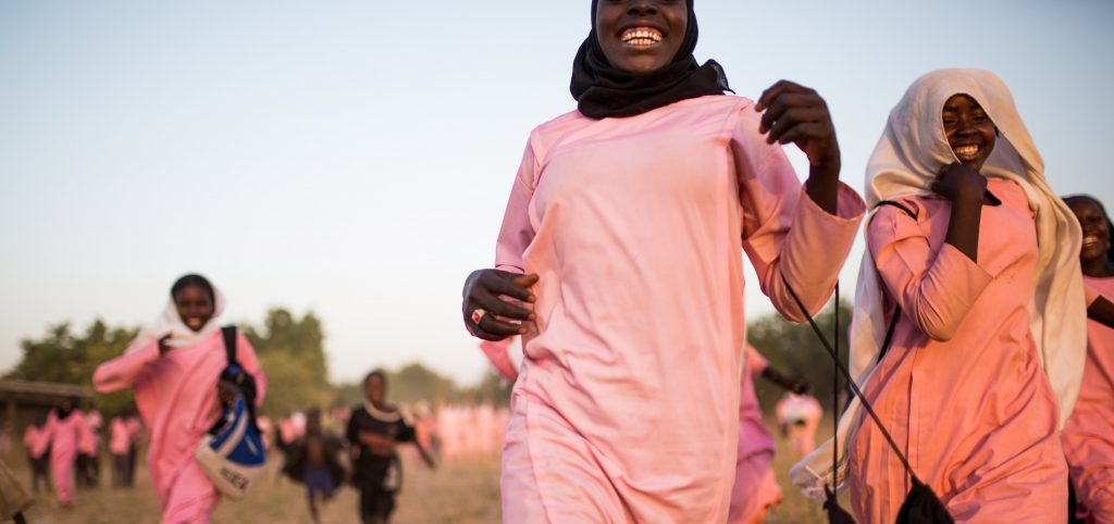 Sudanesiska skolflickor klädda i rosa springer mot kameran.