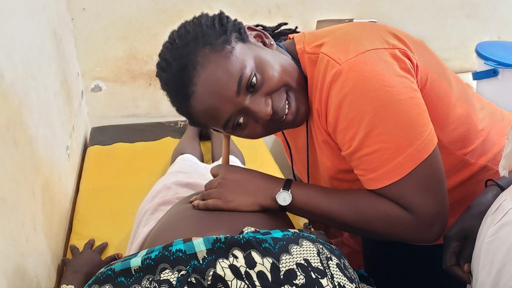 En barnmorska undersöker en patient på en klinik i Sydsudan. Patienten ligger ner på en brits och barnmorskan håller en tratt mot magen och lyssnar.