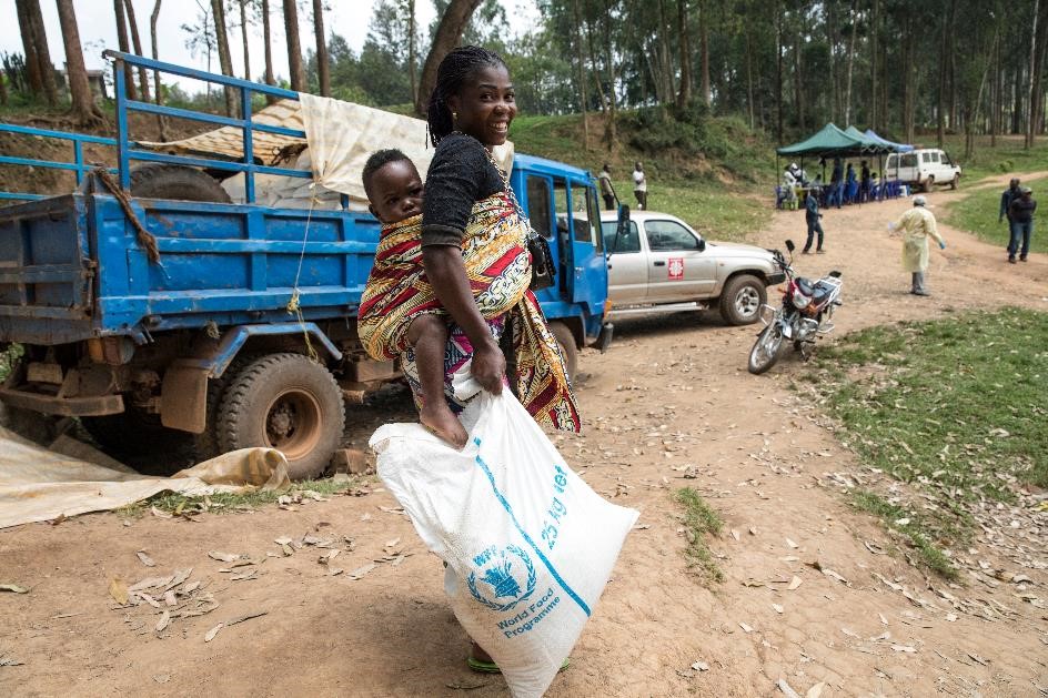 Bilden visar när World Food Programme (WFP) levererar mat till människor som bor i ett område som drabbats av ebola i Demokratiska republiken Kongo 2019. En kvinna bär sitt barn på ryggen och håller i ett av WFP:s matpaket.