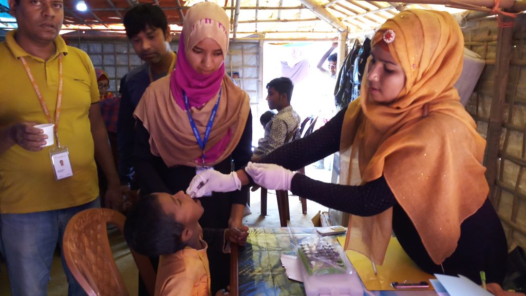 En pojke som sitter på en stol får vaccin av en kvinnlig läkare. I bakgrunden syns tältets väggar, medarbetare och ytterligare en patient.