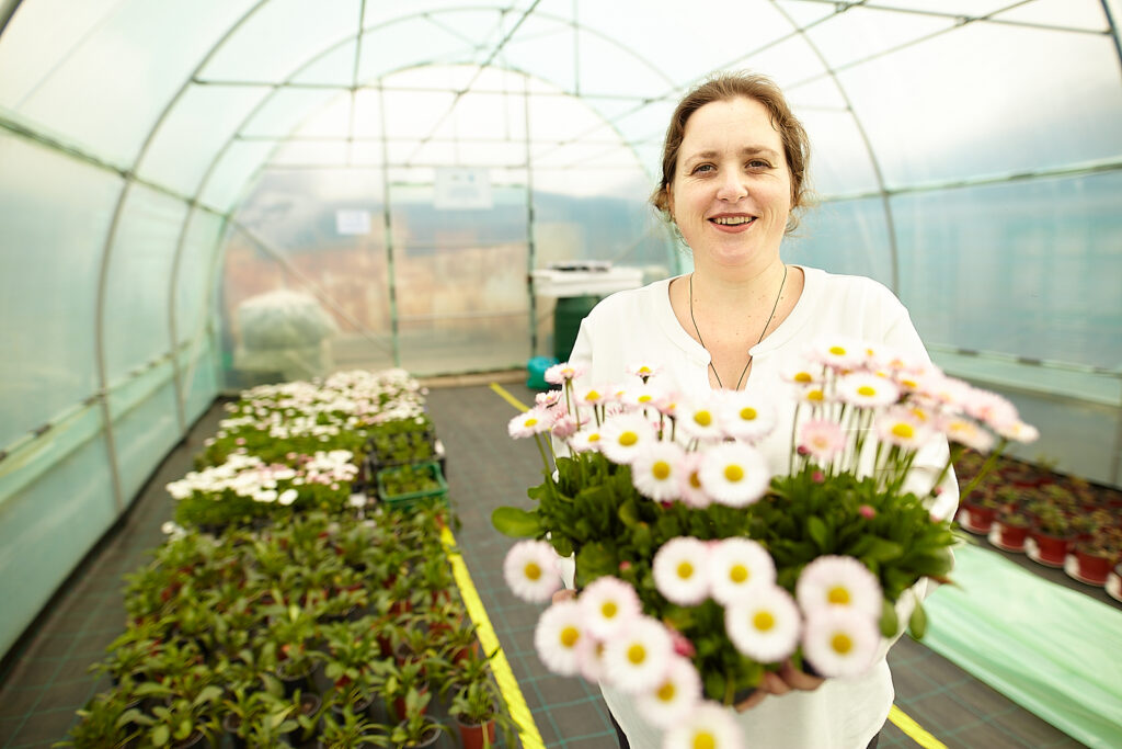 En kvinna håller blommor framför sig och står i ett växthus