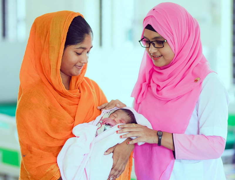 Barnmorska med rosa sjal tillsammans med en mamma och hennes nyfödda barn.