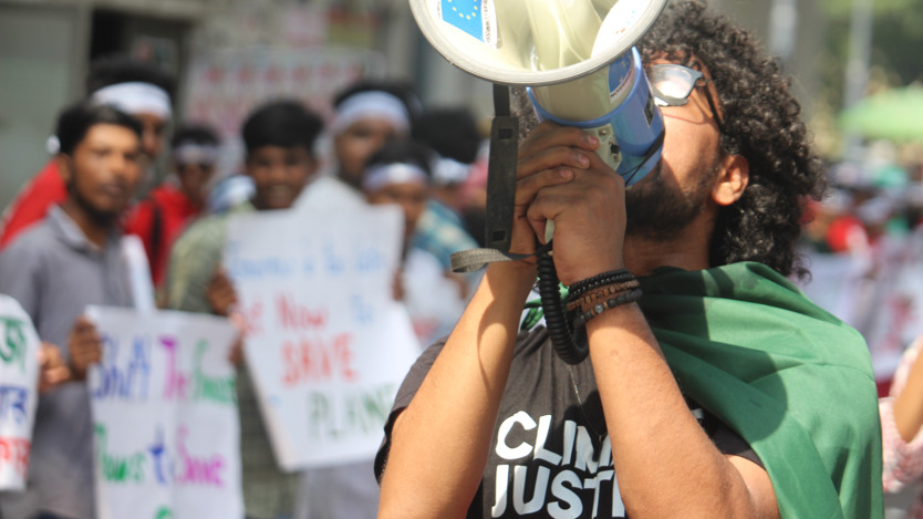 En kille ropar i en megafon. I bakgrunden står människor med plakat.