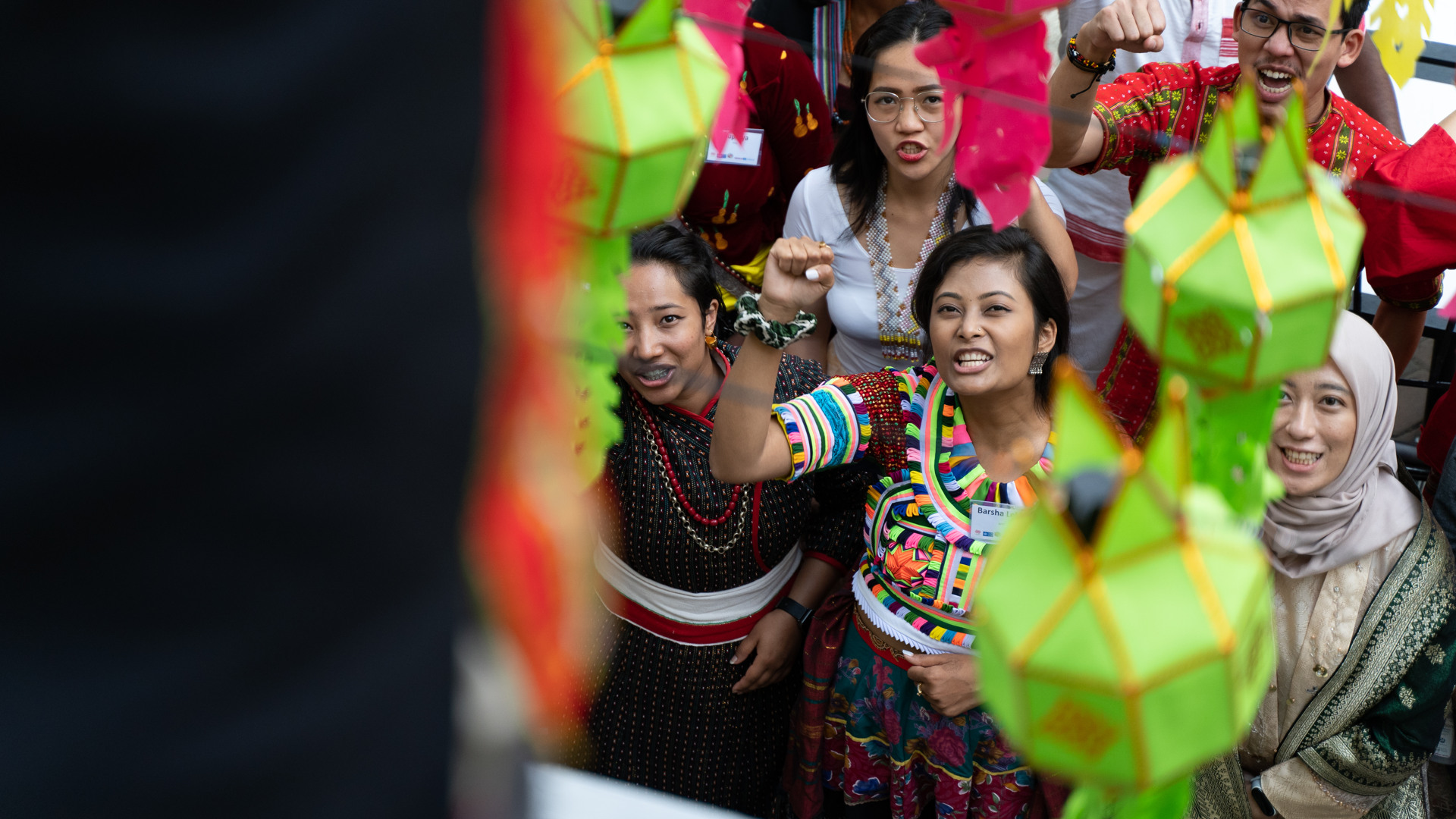 Unga kvinnor och män i olika urfolkskläder lyfter sina nävar och ropar något.