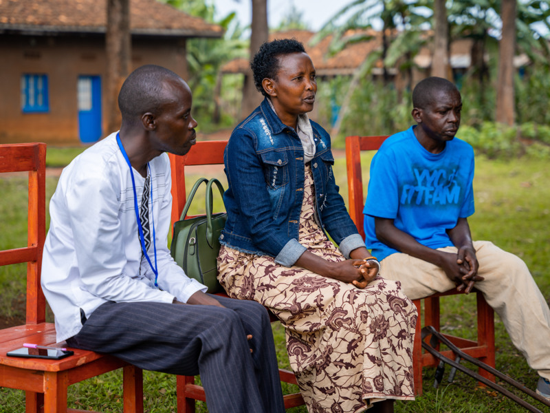 Tre personer sitter utomhus på trästolar.