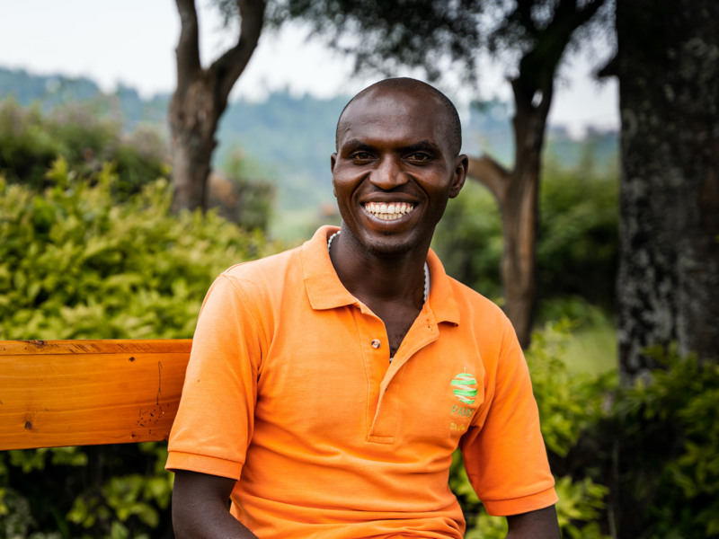 En leende man i orange pikétröja sitter utomhus