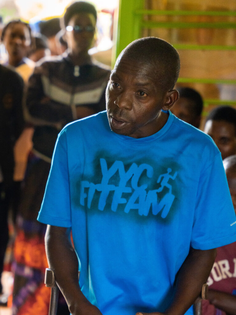 En enbent man står inomhus och berättar något. Han balanserar med hjälp av ett par kryckor.