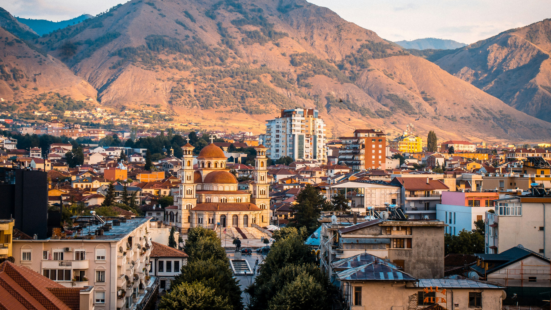En stad sedd snett ovanifrån. Ett myller av olika byggnader. I bakgrunden finns höga berg.