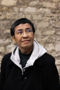 En kvinna blickar snett uppåt. En murad vägg i bakgrunden.