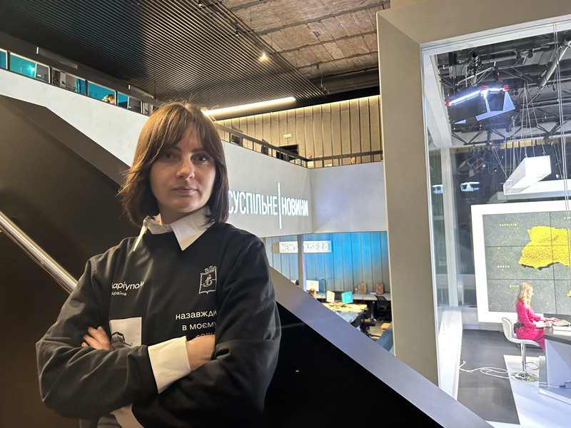 En ung kvinna står med armarna i kors framför en nyhetsstudio.