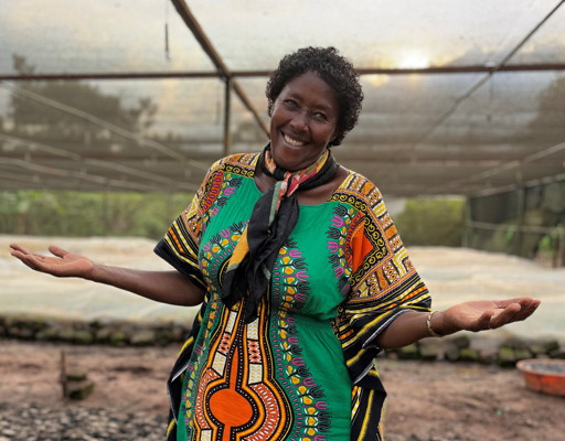 Smiling woman in patterned dress with arms out, showing her plant nursery