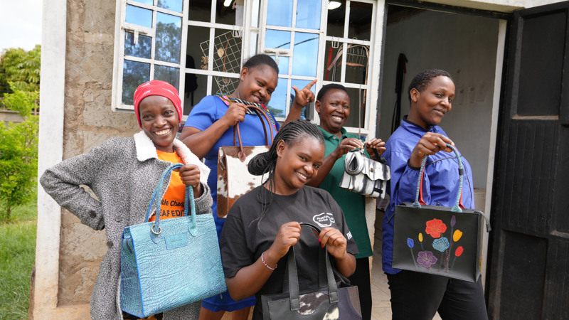 Fem kvinnor i grupp ler och håller i läderväskor.