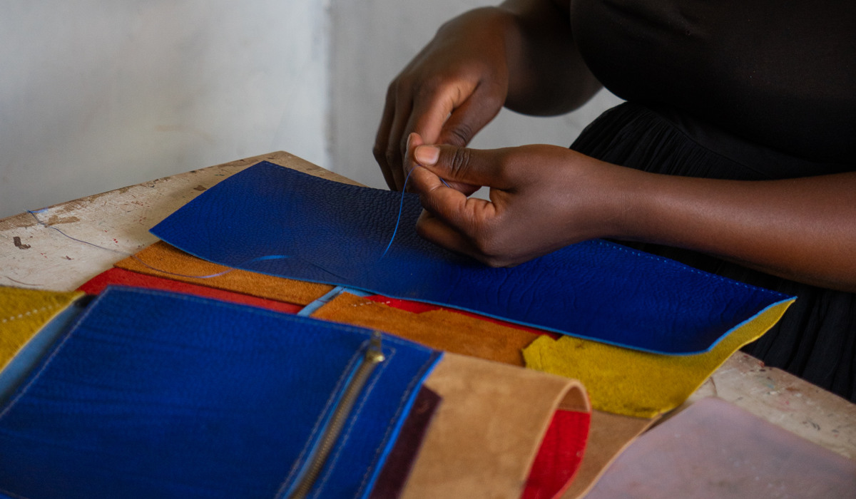 Två händer som syr i blått läder.