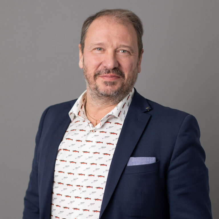 Närbild på man i mörk kavaj och mönstrad vit skjorta.