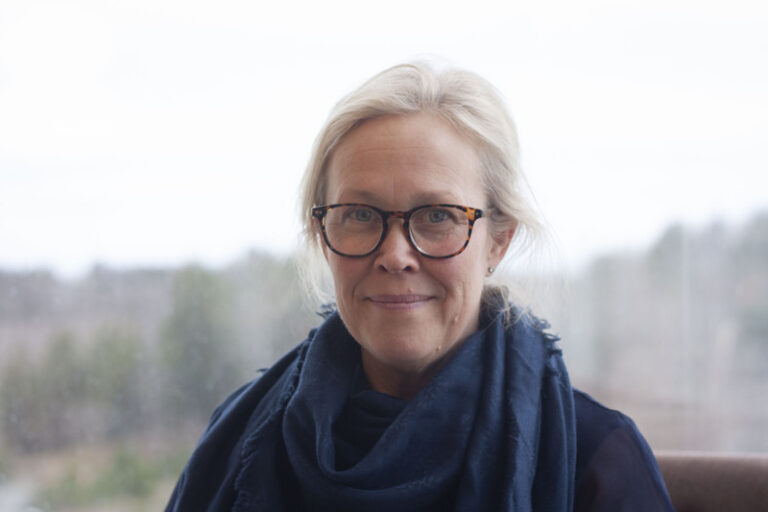 Porträtt på kvinna i glasögon och scarf med bakgrund i oskärpa.