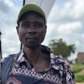 En man klädd i brokig skjorta och keps poserar i Zimbabwe.