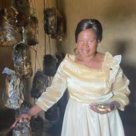 kvinna i fin klänning pekar på sin svampskörd som hänger på tork längs väggen.