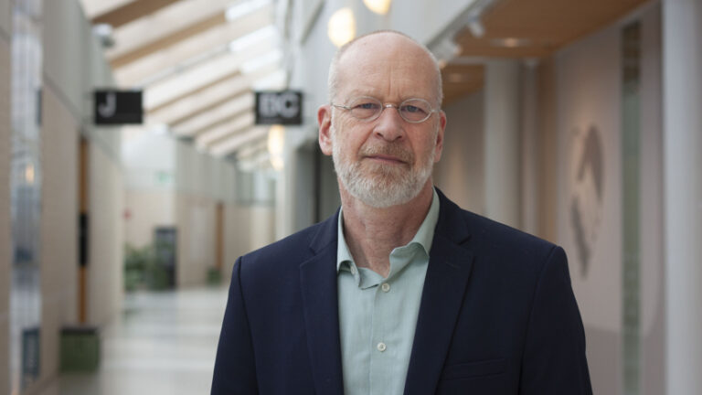 Närbild på man i glasögon, mörk kavaj och ljus skjorta.