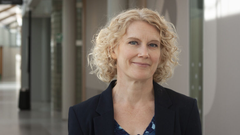 Porträtt på kvinna i axellångt, ljust krulligt hår och svart kavaj.