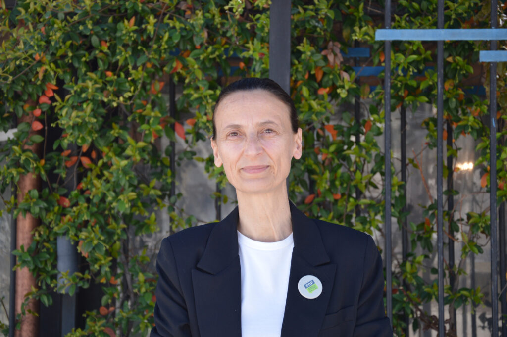 En kvinna i svart kavaj som står framför en vägg med växter.