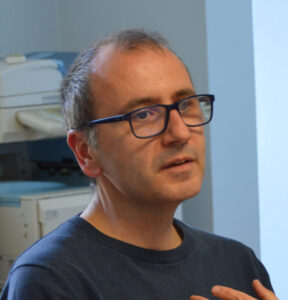 En man som sitter vid ett skrivbord och ser ut att berätta något.