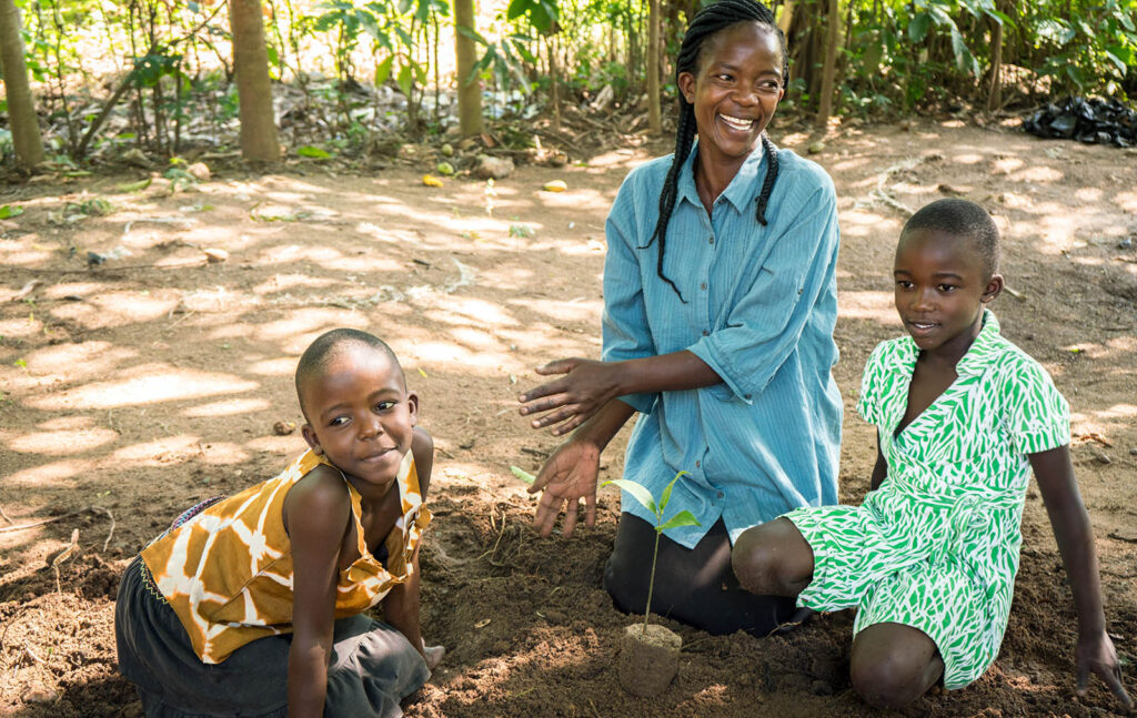 Mamma Lilian Ochieng med barnen Frida och Eliezel, planterar träd på sin gård i Kisumu, Kenya