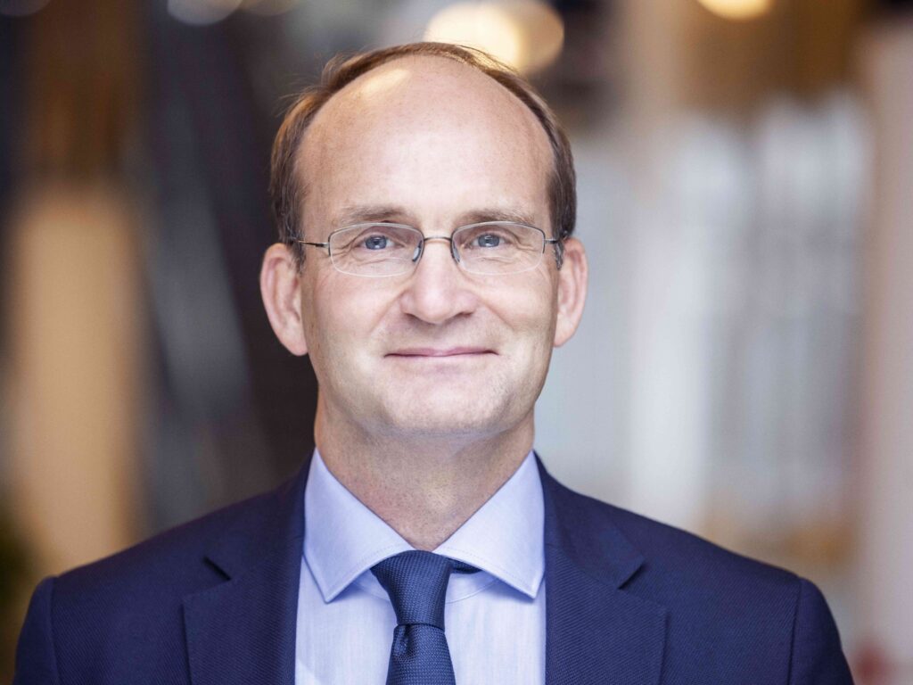 En man i kavaj, skjorta och slips framför en suddig bakgrund