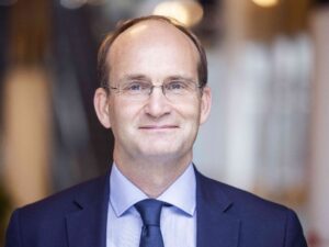 En man i kavaj, skjorta och slips framför en suddig bakgrund