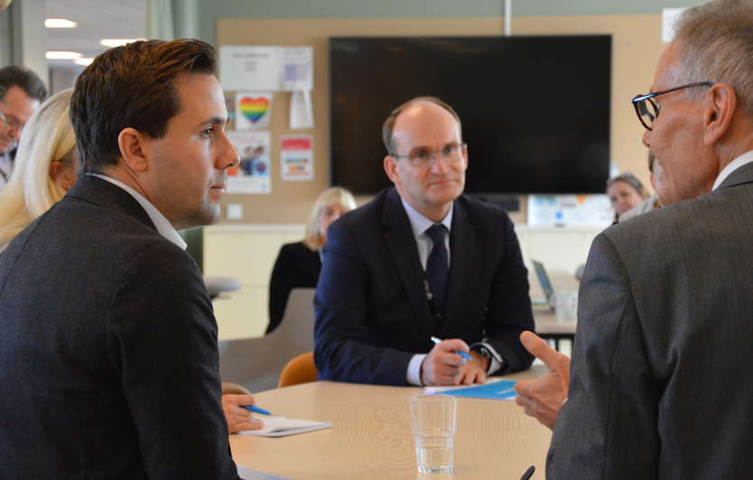 Benjamin Dousa, Erik Korsgren och Jakob Granit samtalar vid ett bord. Andra personer lyssnar också omkring.