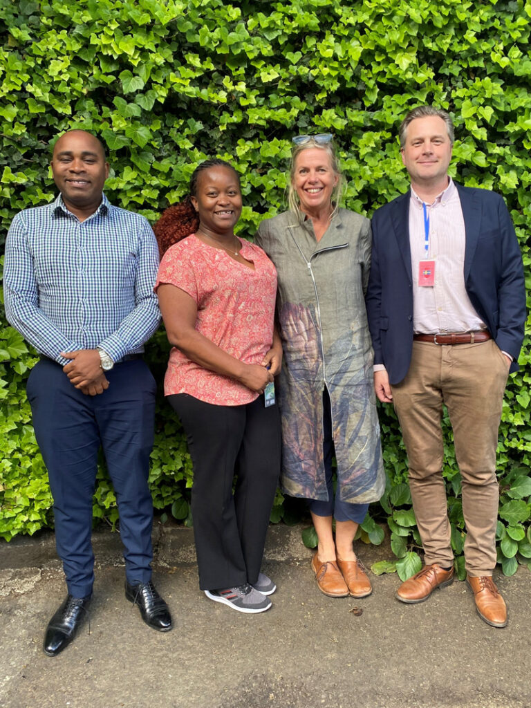 Fyra personer poserar framför en grön häck.