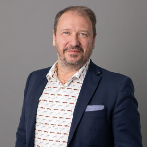 Närbild på man i mörk kavaj och mönstrad vit skjorta.