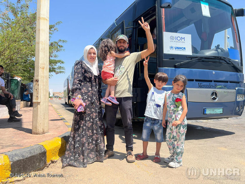 En man och en kvinna står framför en buss med tre barn, ett av dem håller mannen i sin famn.