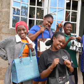 Fyra kvinnor håller i läderväskor och ser glada ut.