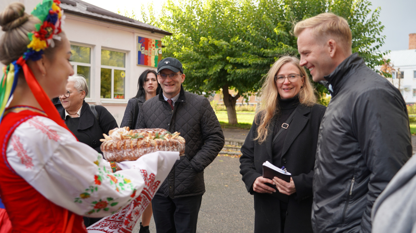 En grupp människor som möts av en traditionellt klädd Ukrainare som bjuder på kaka.