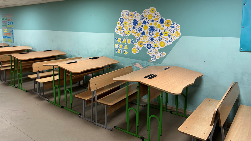Ett klassrum med träbänkar och en väggmålning.