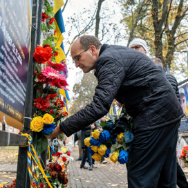 En man lägger blommor på en minnesvägg.