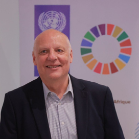 En man med kostym och skjorta med en skylt i bakgrunden med de globala målen.