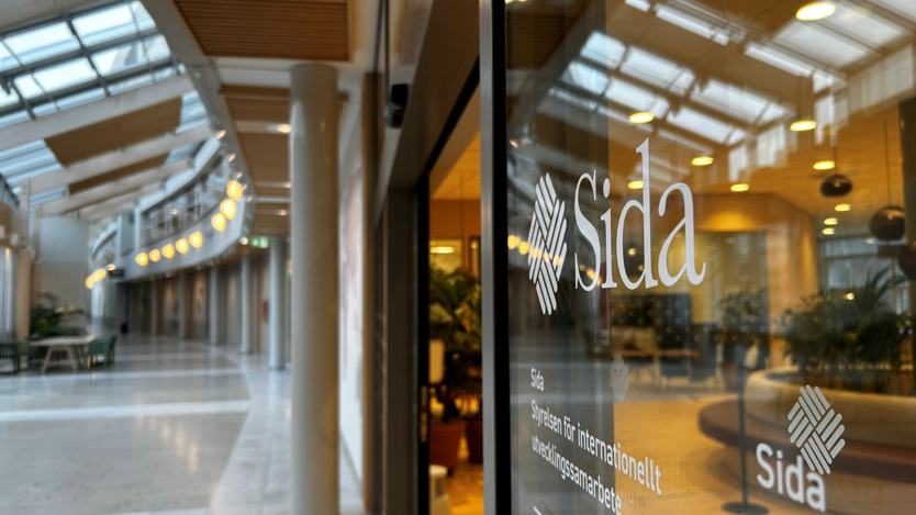 Sodas logotyp på en glasruta som visar en reception innanför och en korridor utanför. 