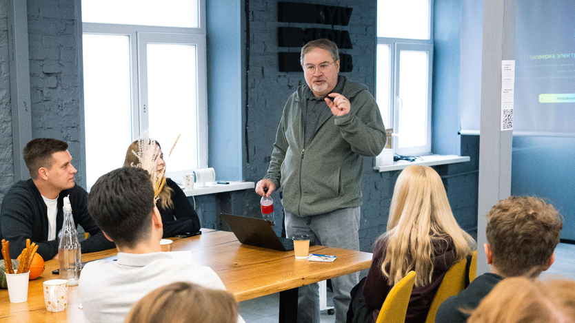 Man står inför personer sittande runt bord.