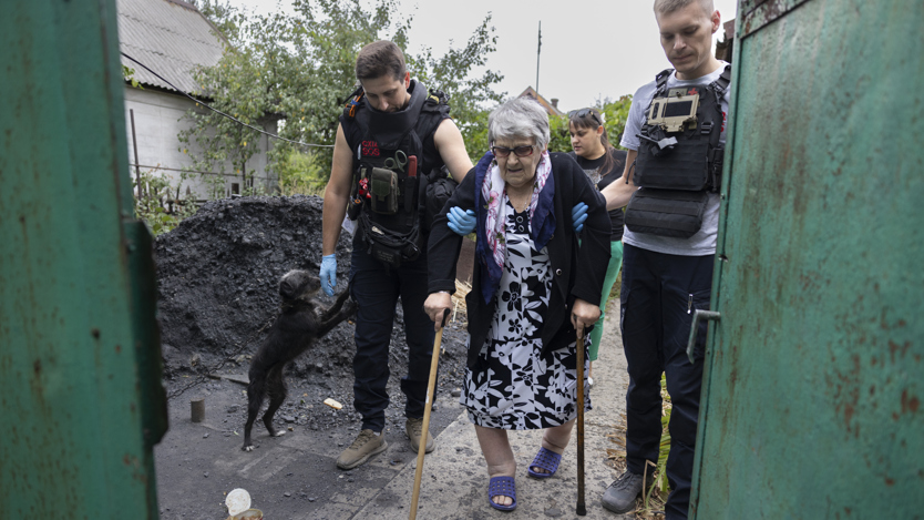 En kvinna med kryckor får hjälp av två män. 