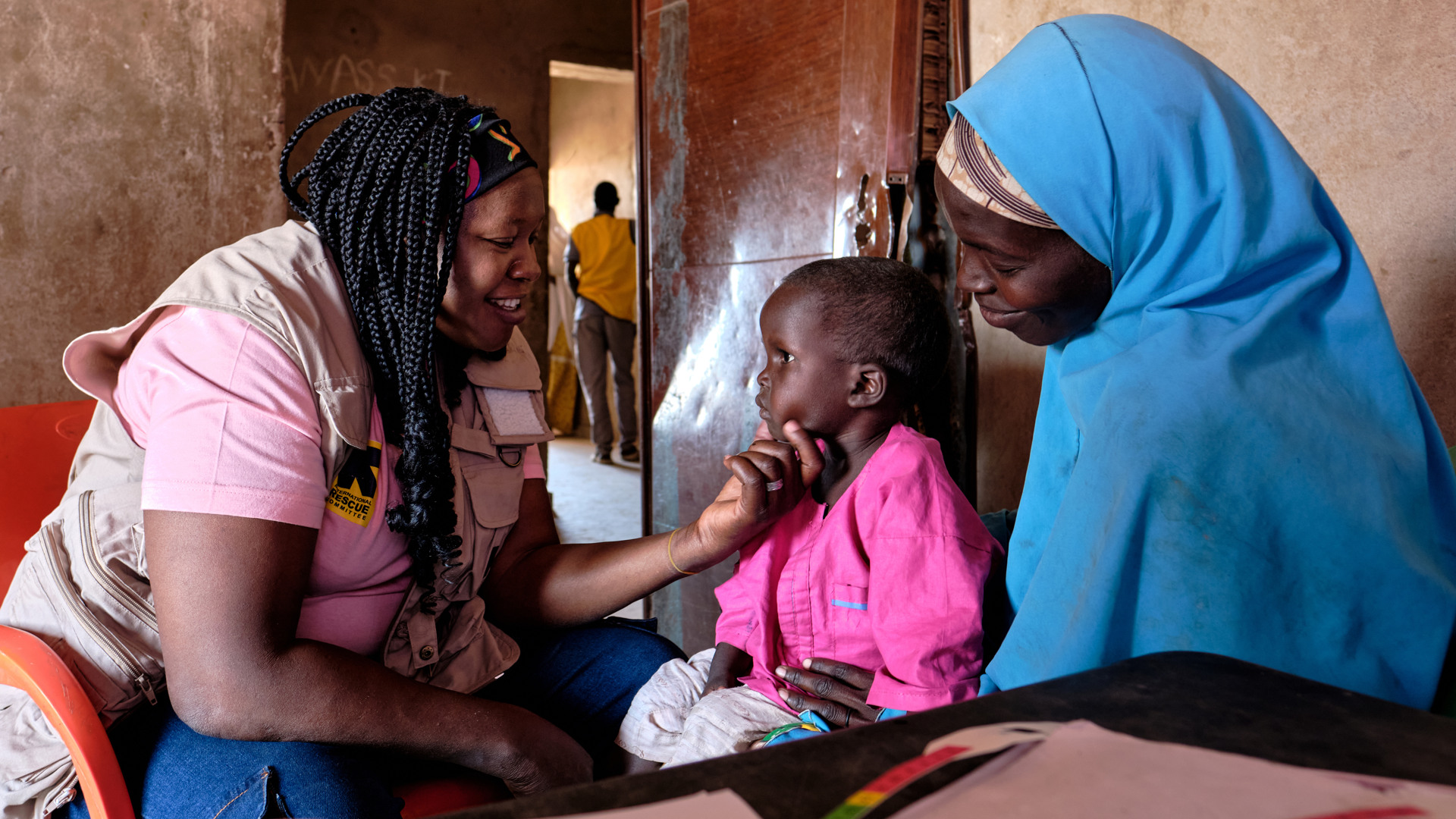 En kvinna undersöker en liten flicka som sitter i sin mammas knä.