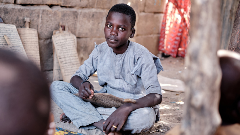 En ung pojke sitter på marken framför en mur.