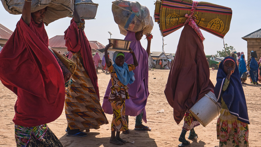 En grupp kvinnor och barn bär på stora bylten och hinkar på sina huvuden.
