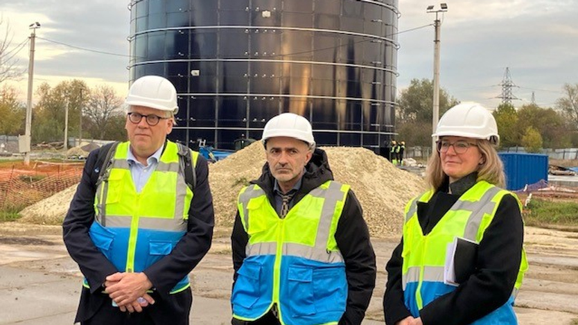 Två män och en kvinna  i arbetshjälmar i på en industriplats. 