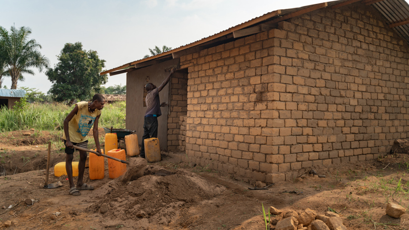 Två personer bygger på ett litet hus i tegel.