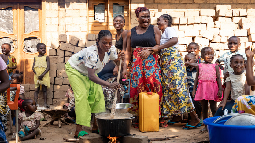 En grupp kvinnor och barn som står runt en eld och lagar mat.