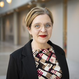 Porträtt i halvfigur på kvinna i mönstrad klänning och svart kavaj.