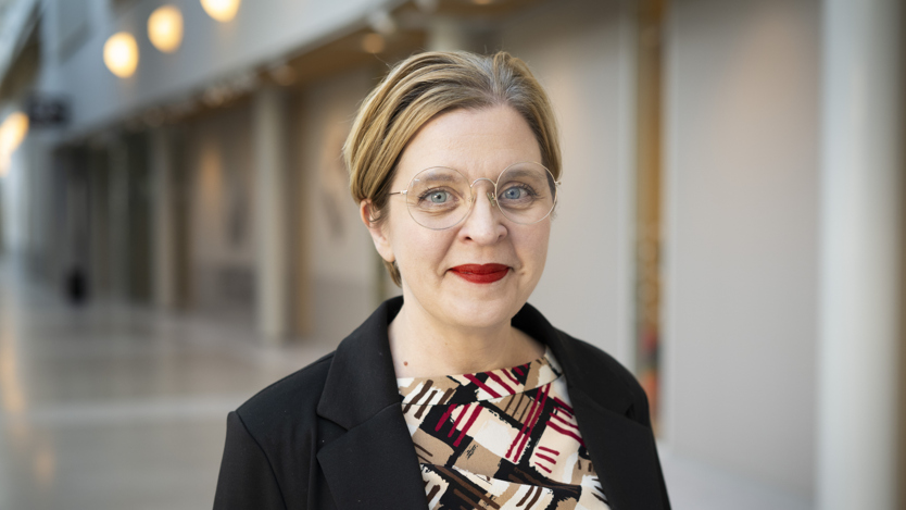 Porträtt i halvfigur på kvinna i mönstrad klänning och svart kavaj.