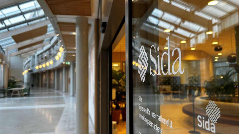 Sodas logotyp på en glasruta som visar en reception innanför och en korridor utanför. 
