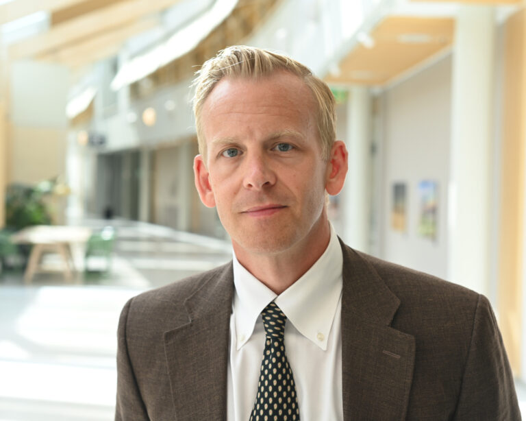 Porträtt av blond man i kavaj och slips. 